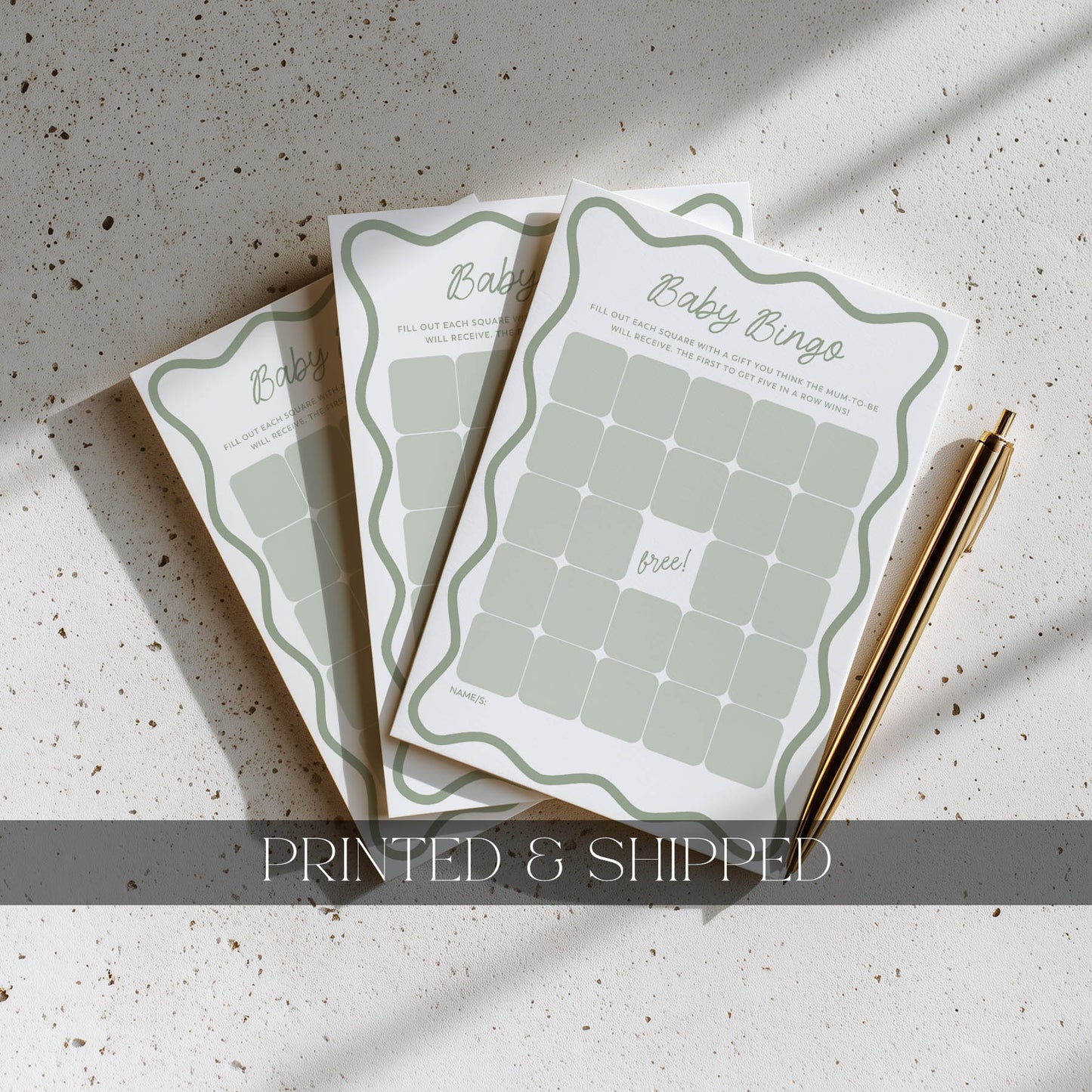 Three baby bingo cards on a textured surface with a pen next to them, labeled 'Printed & Shipped'.