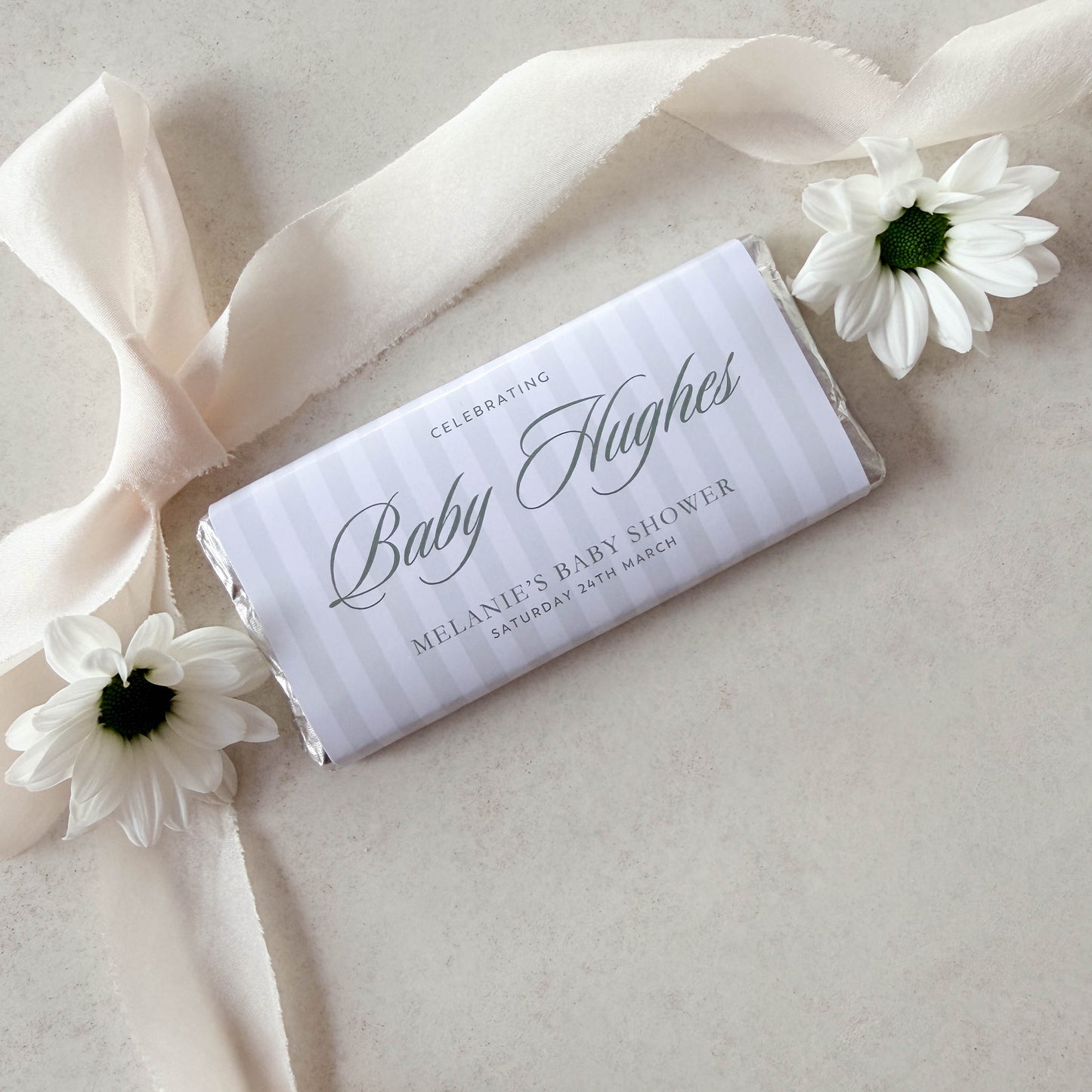 Personalized baby shower chocolate bar with ribbon and flowers on a light background