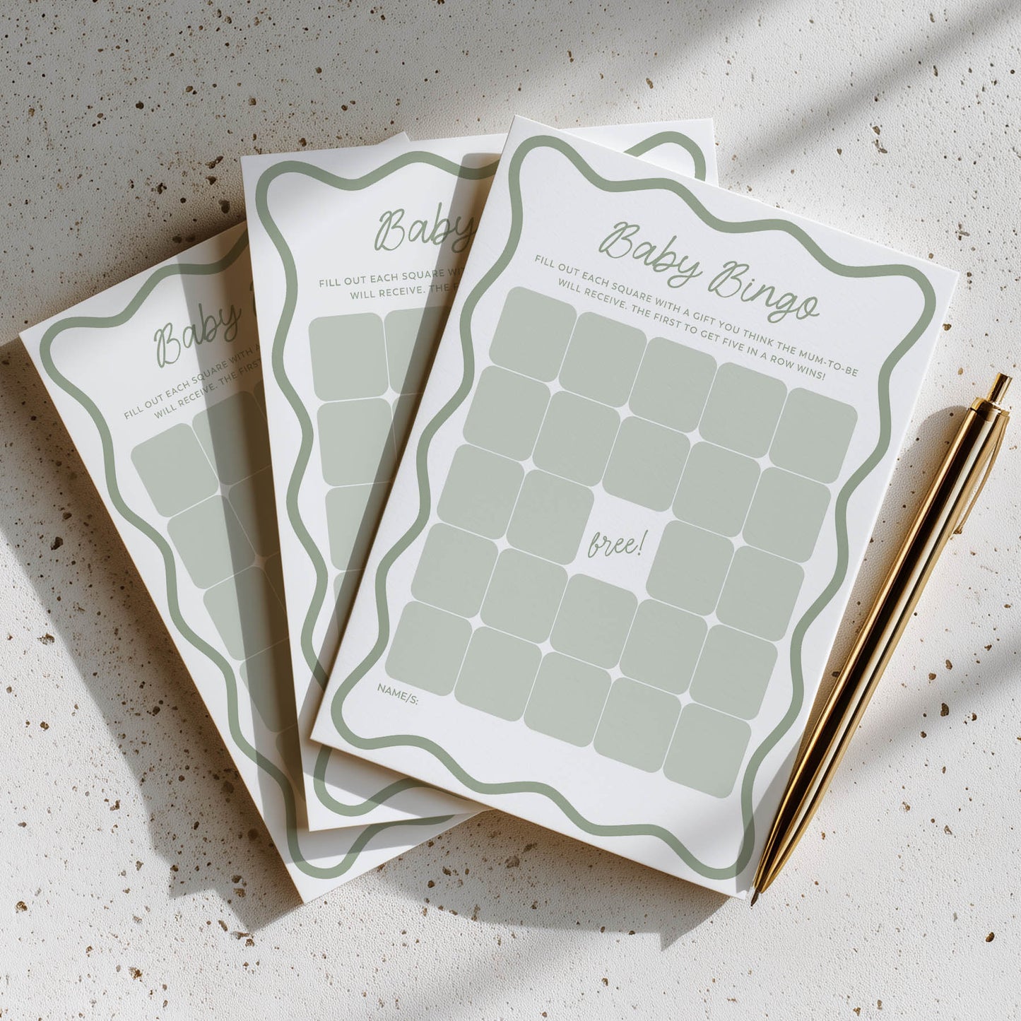 Three baby shower bingo cards on a textured surface with a pen.