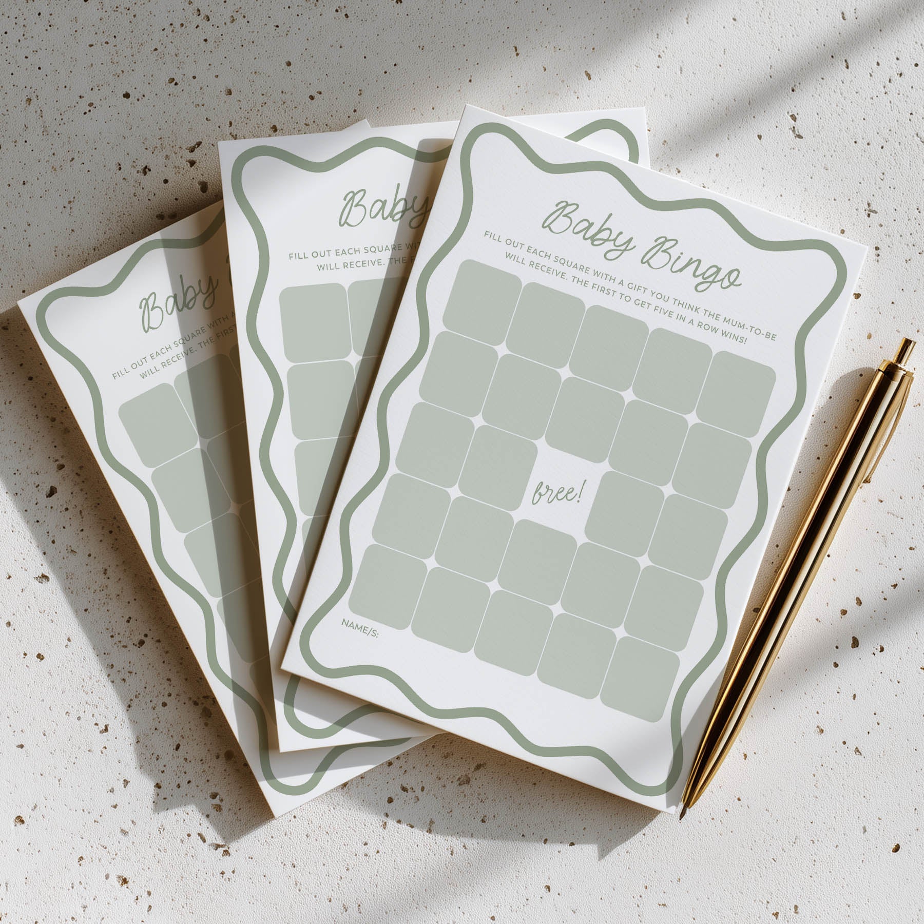 Three baby shower bingo cards on a textured surface with a pen.