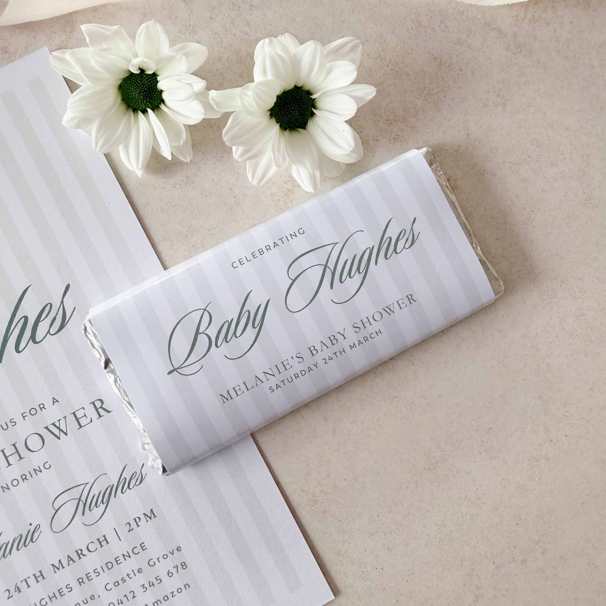 Baby shower invitation with a bar of chocolate and white flowers on a beige background