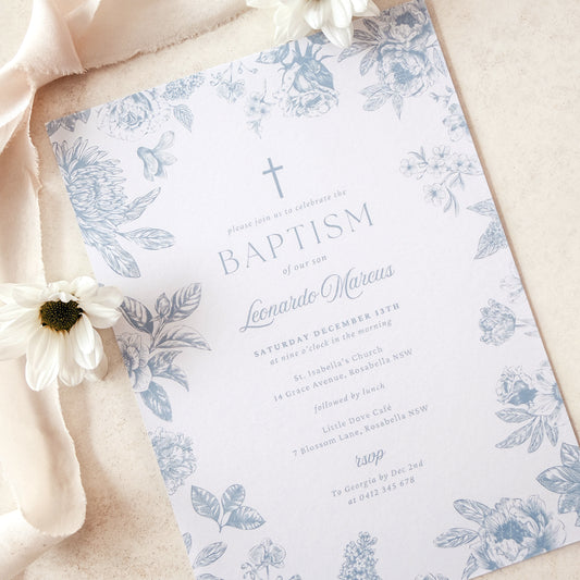 Baptism invitation with floral design and cross, placed on a soft fabric background.