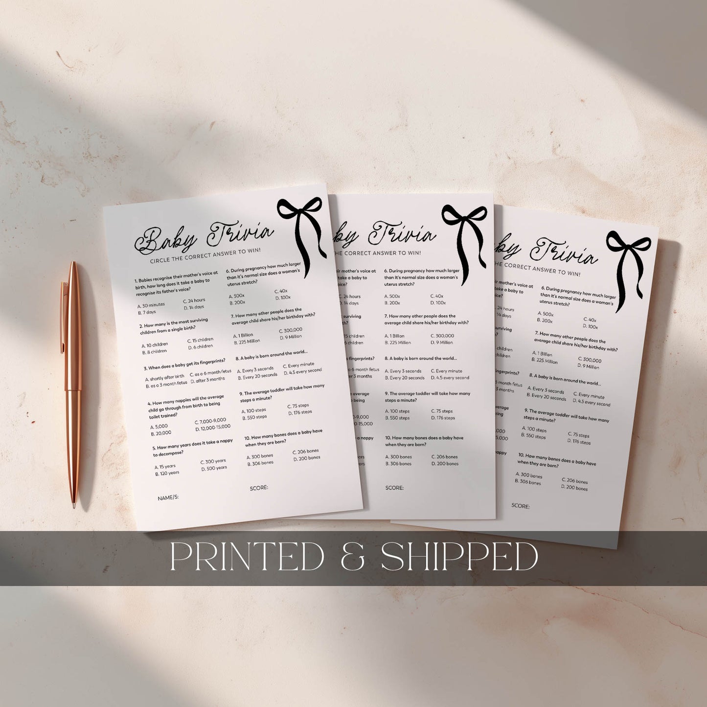 Three black bow printed baby trivia cards with a pen on a light surface, labeled 'Printed & Shipped'.