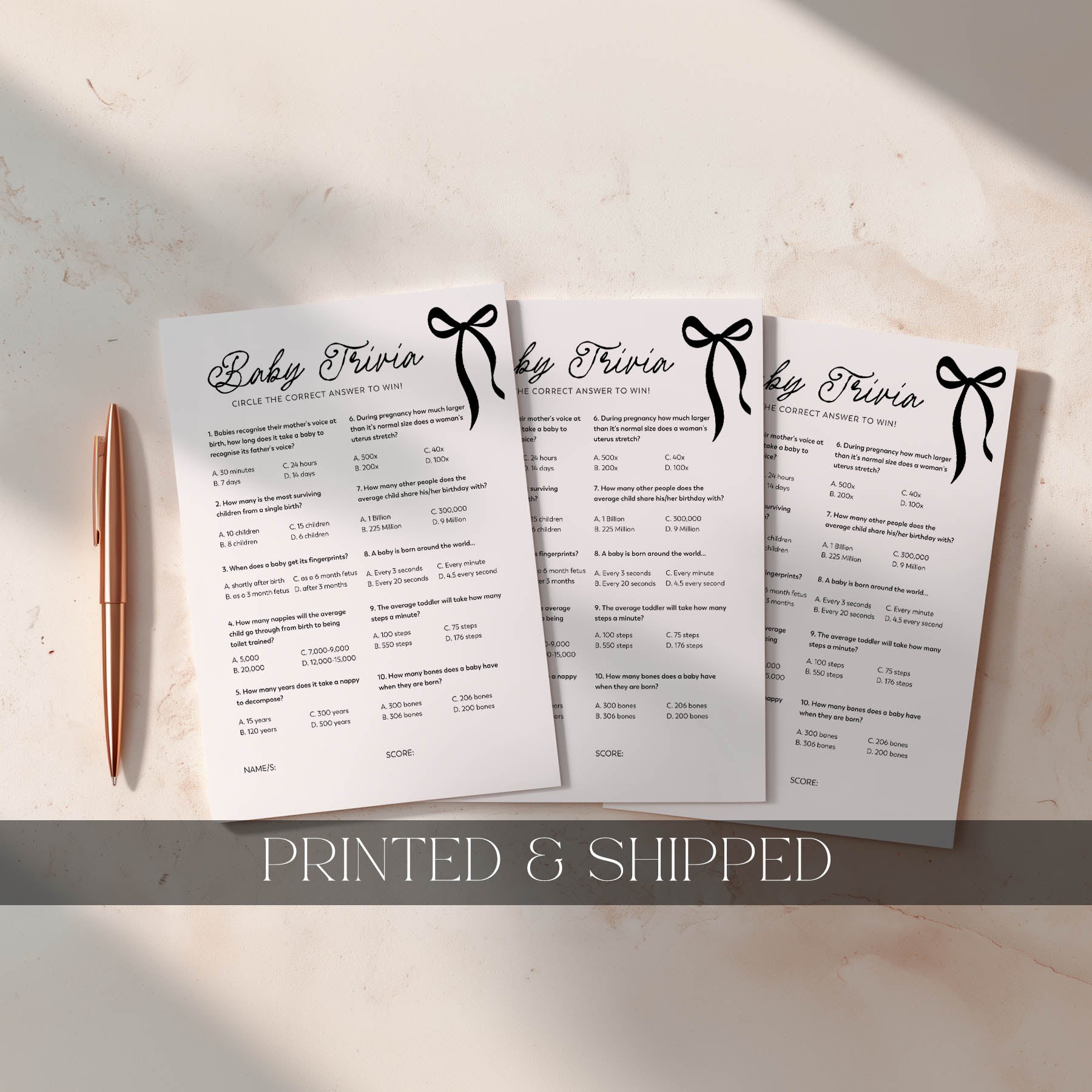 Three black bow printed baby trivia cards with a pen on a light surface, labeled 'Printed & Shipped'.