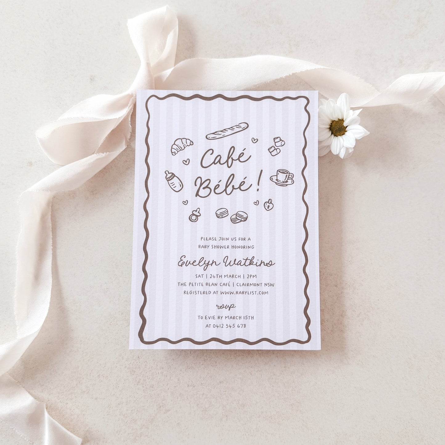Baby shower invitation card on a light fabric background with a white flower.