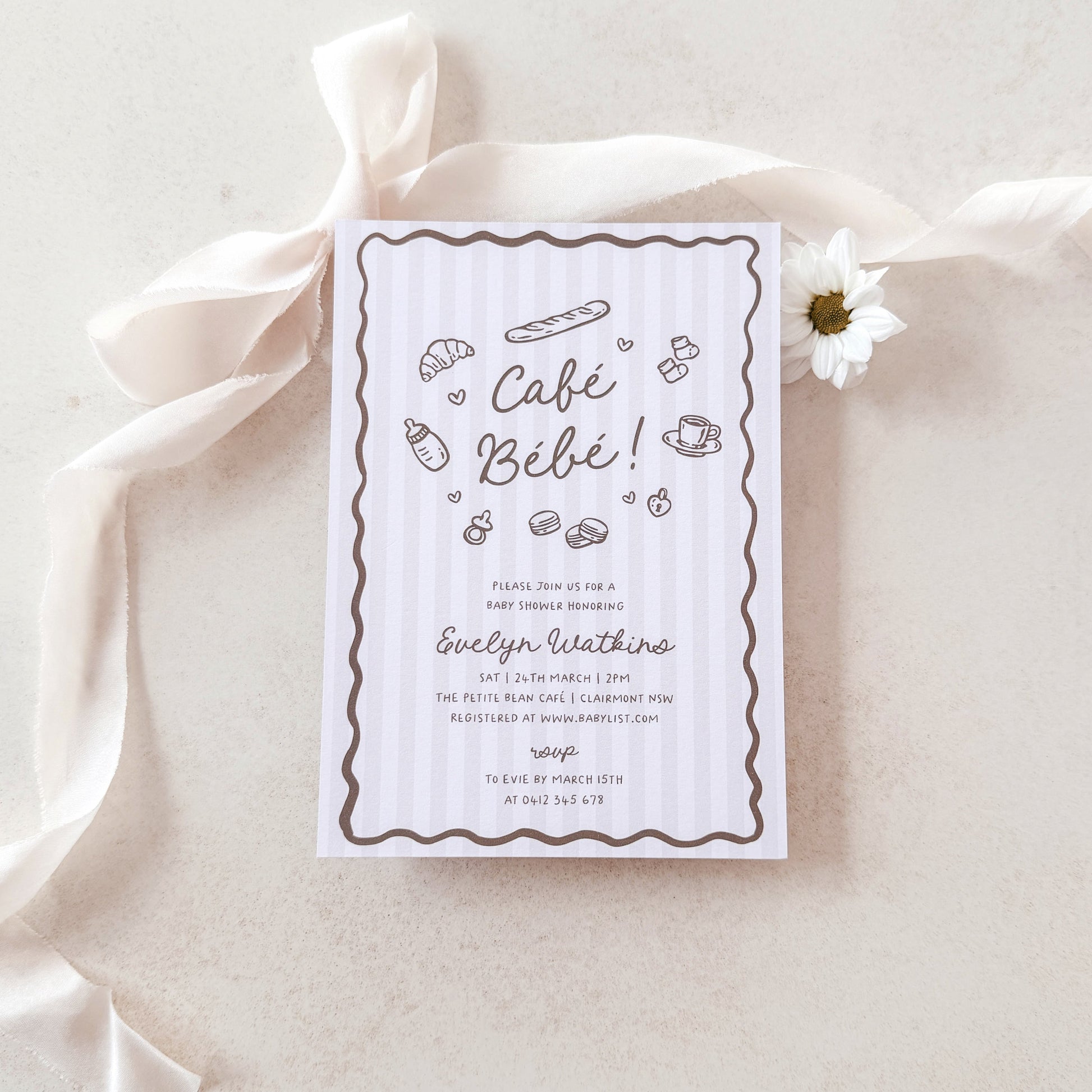 Baby shower invitation card on a light fabric background with a white flower.