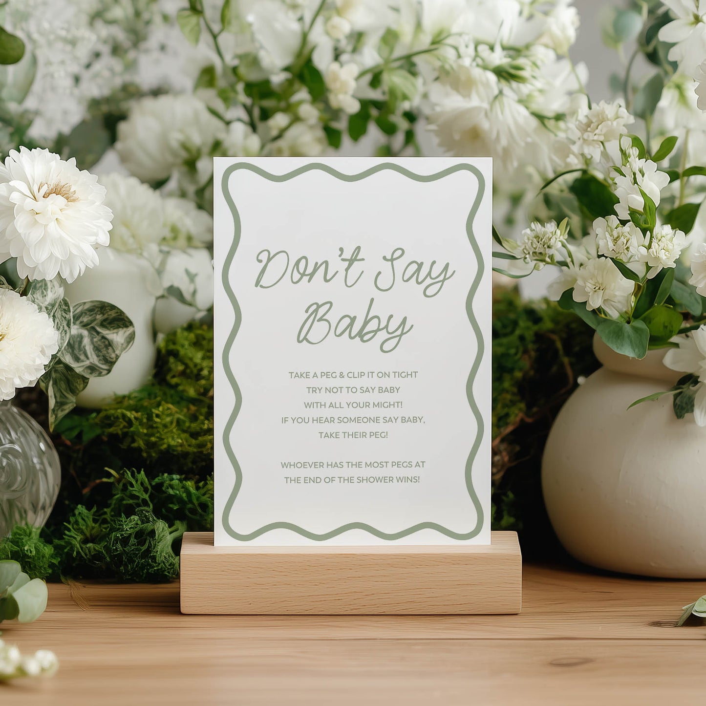 Decorative green wavy sign with 'Don't Say Baby' text in a floral setting