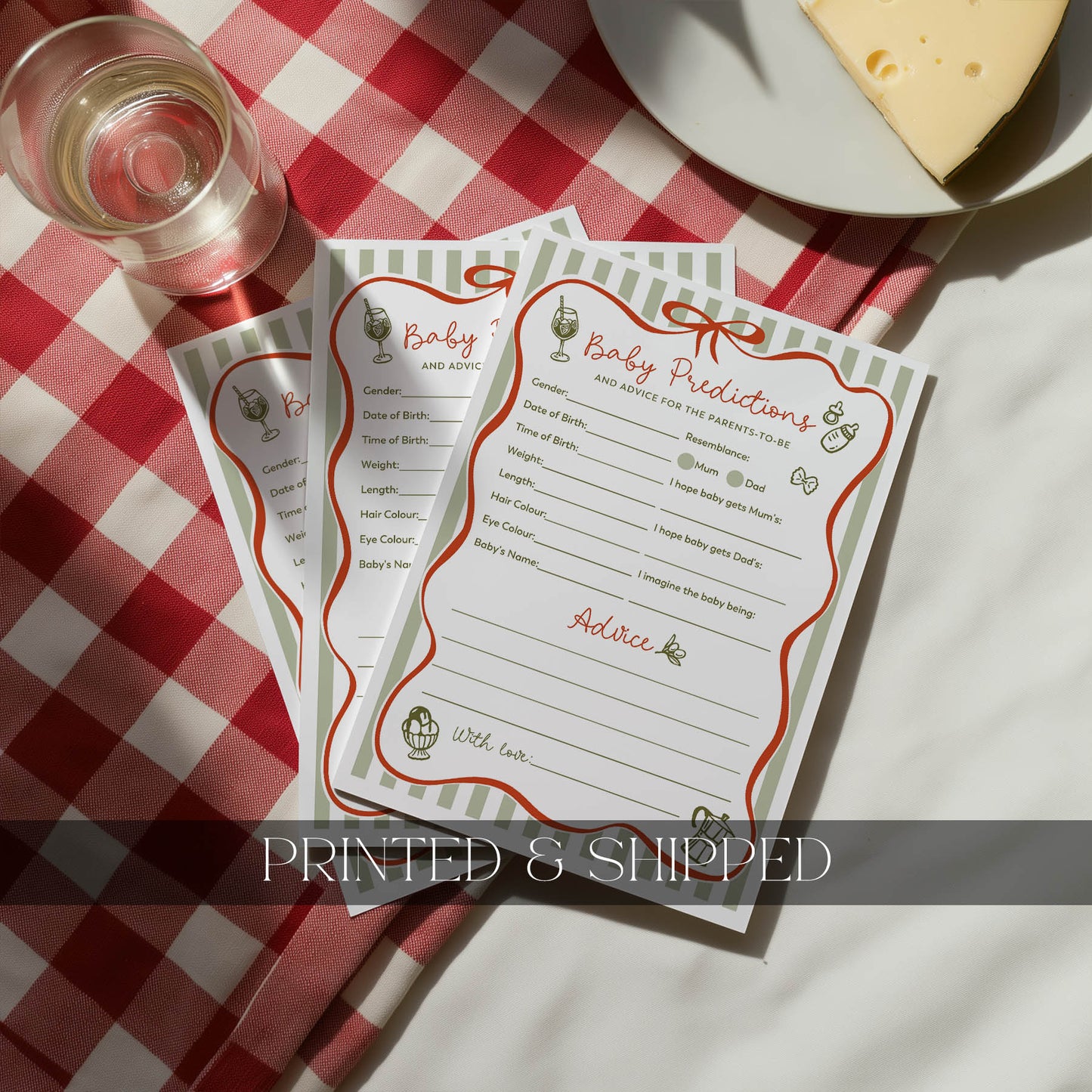 Baby shower game cards on a red and white checkered tablecloth with a glass of wine and cheese.