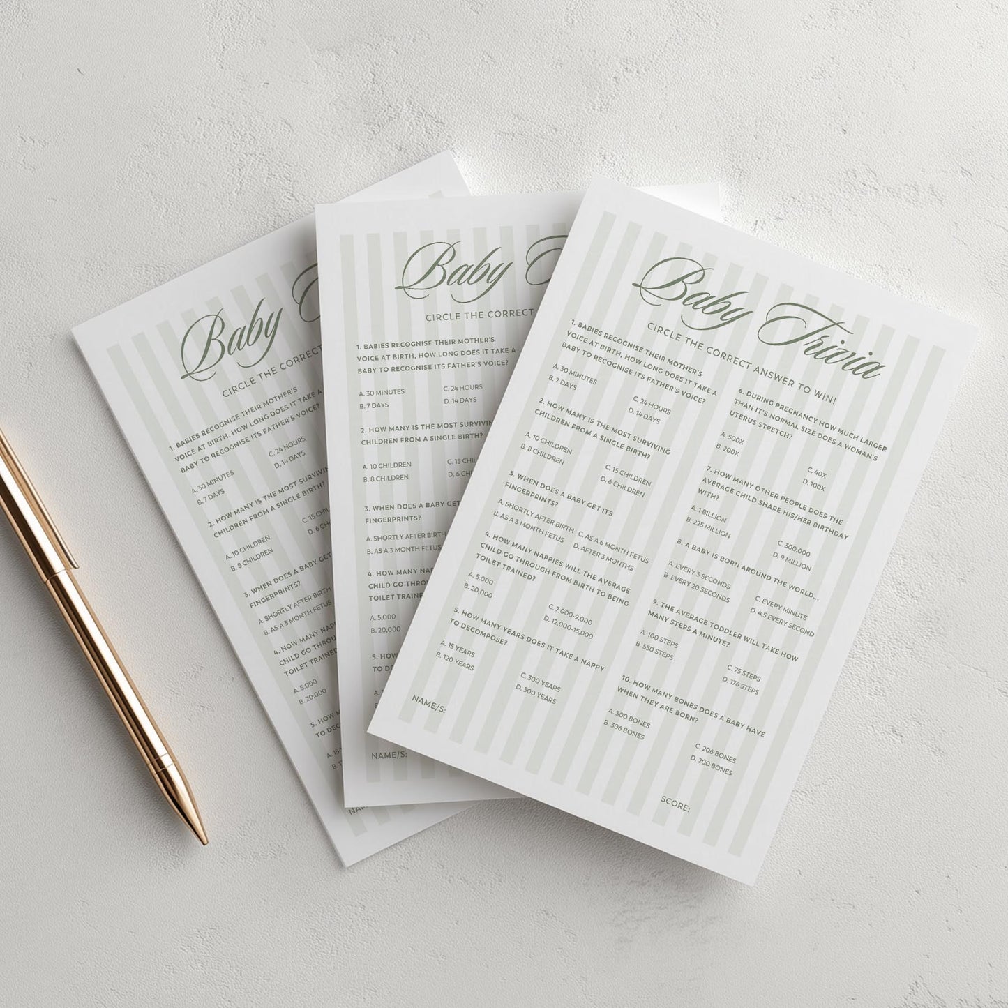 Three green stripe baby shower invitations on a light gray surface with a pen.