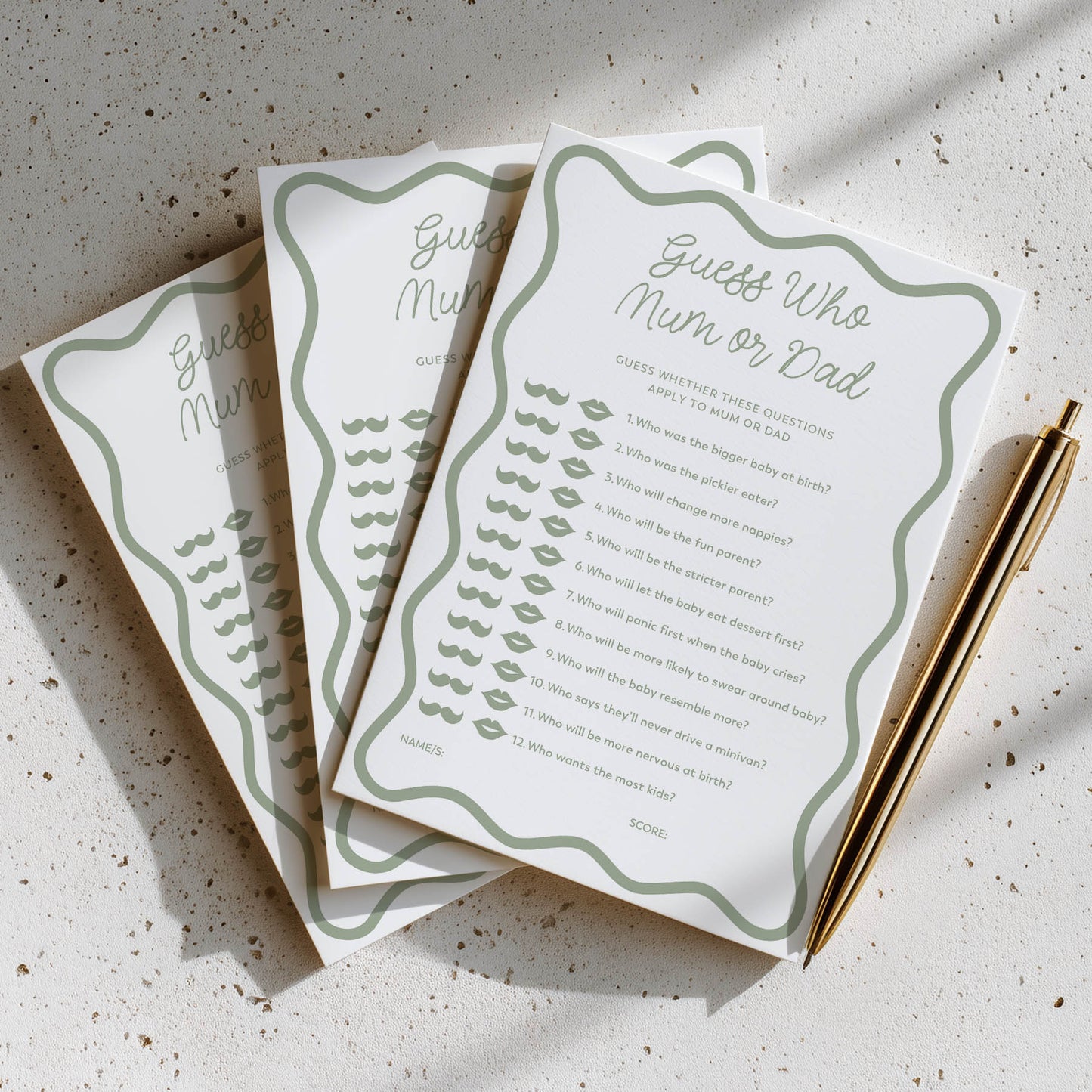 Three baby shower game cards titled 'Guess Who Mum or Dad' on a textured surface with a pen.