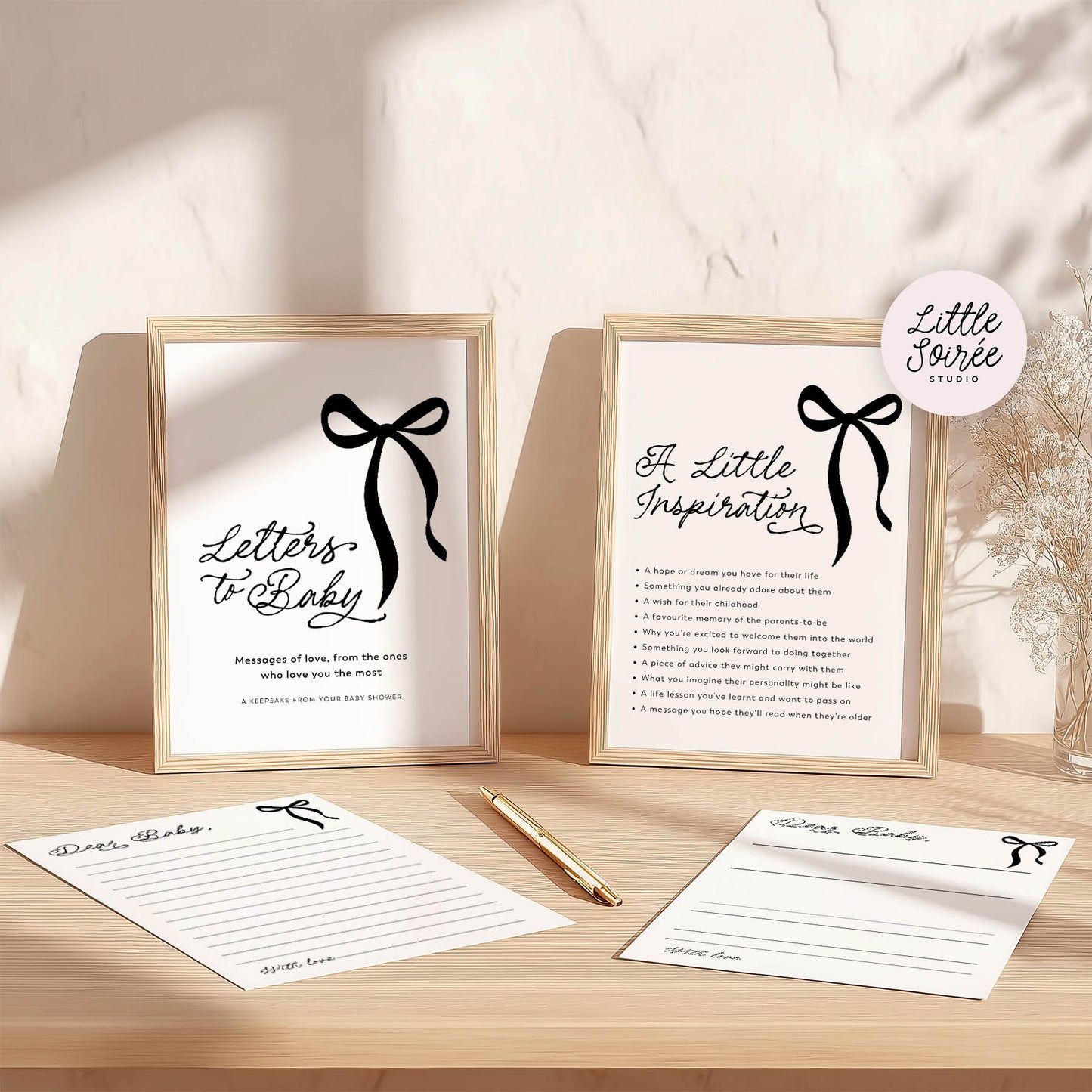 Two framed prints with text and a black bow design on a wooden surface with stationery items.