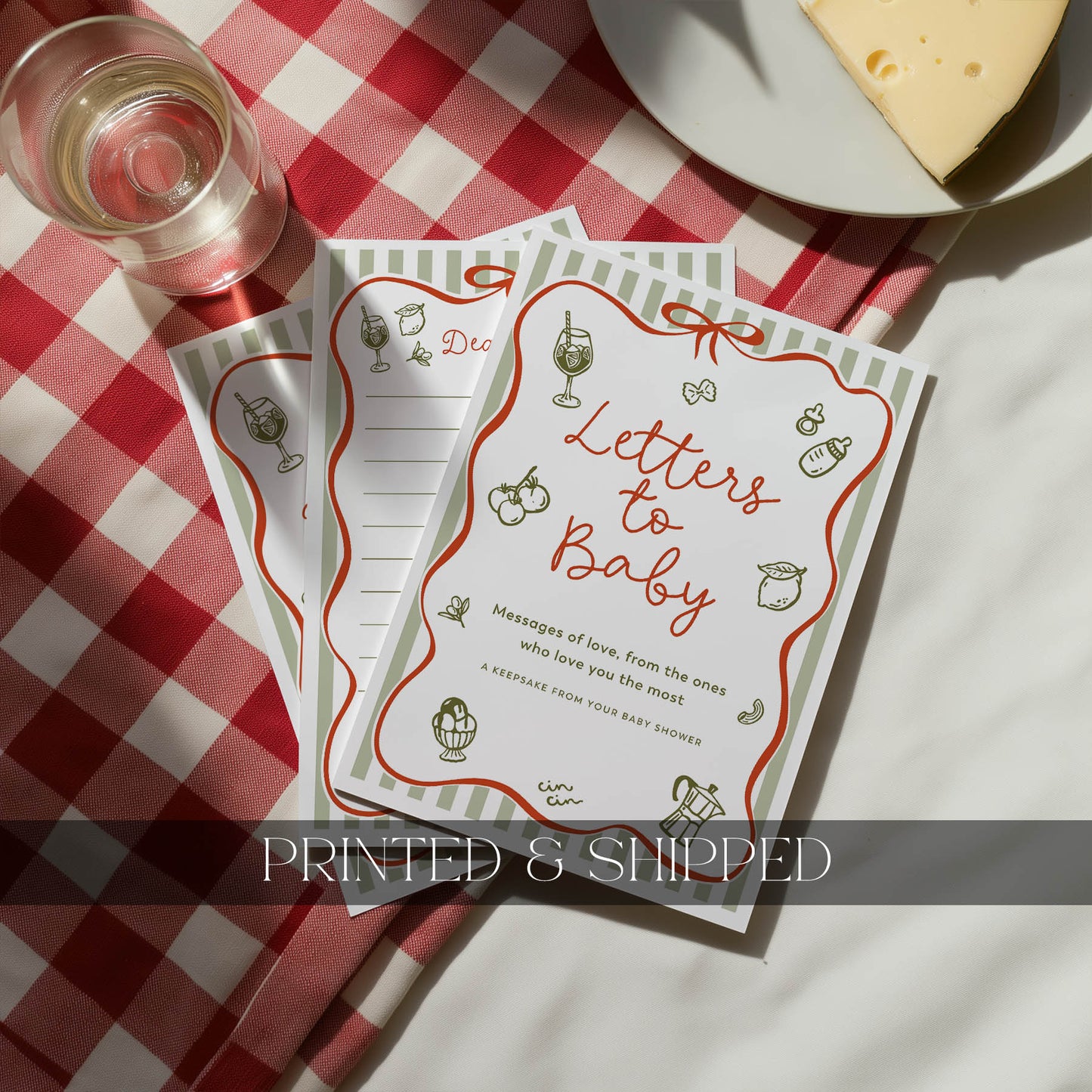 Two 'Letters to Baby' cards on a red and white checkered tablecloth with a glass of wine and cheese.