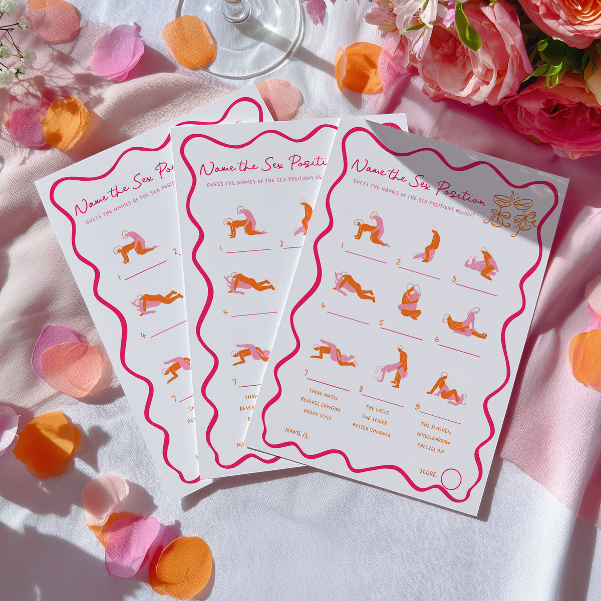 Three printed cards titled "Name the Six Poses" are arranged on a white fabric surface with pink and orange flower petals and flowers around them. The cards show illustrated yoga poses in pink, orange, and purple tones with short descriptions.