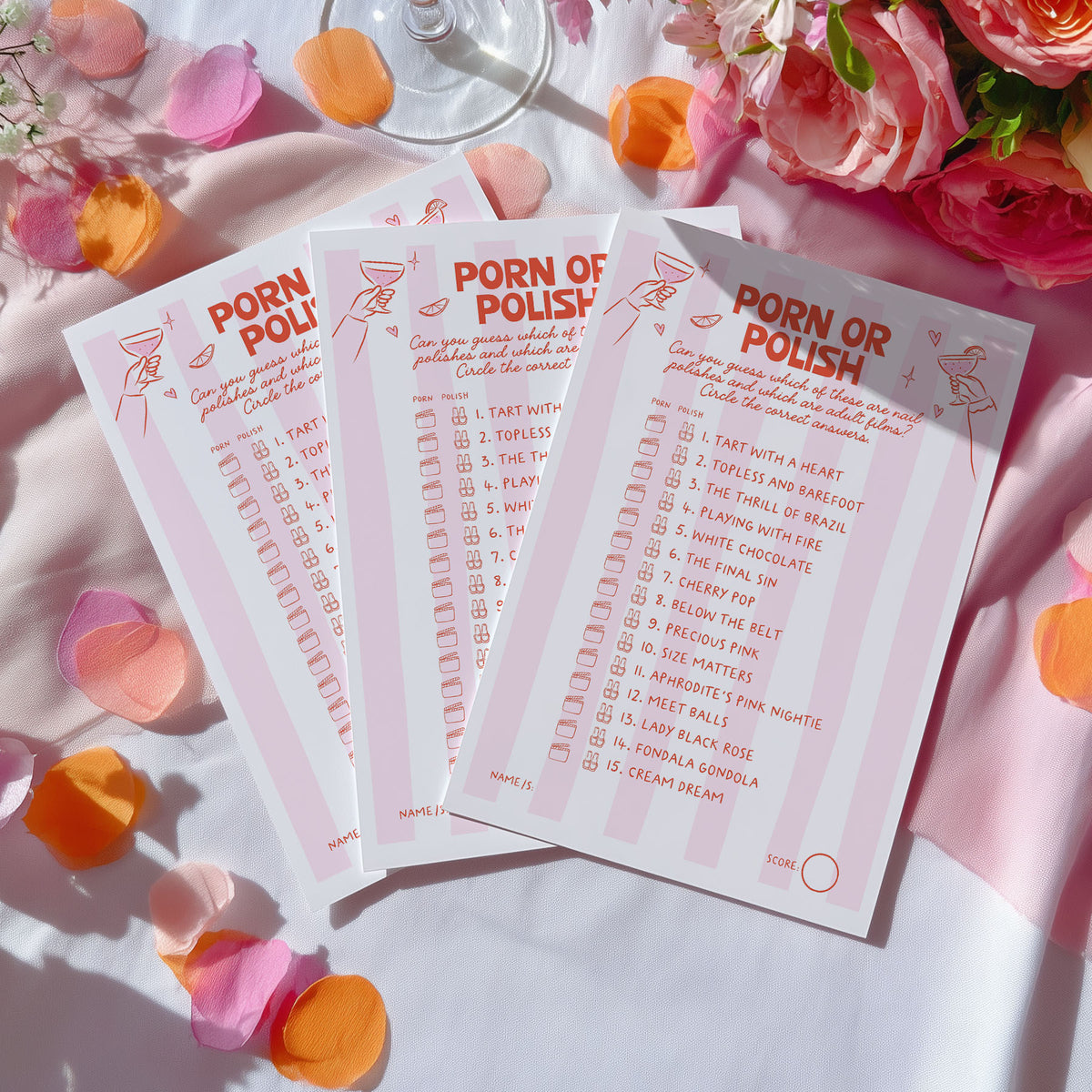 Three pink printed cards titled "PORN OR POLISH" arranged on a white surface with scattered rose petals and flowers around them.