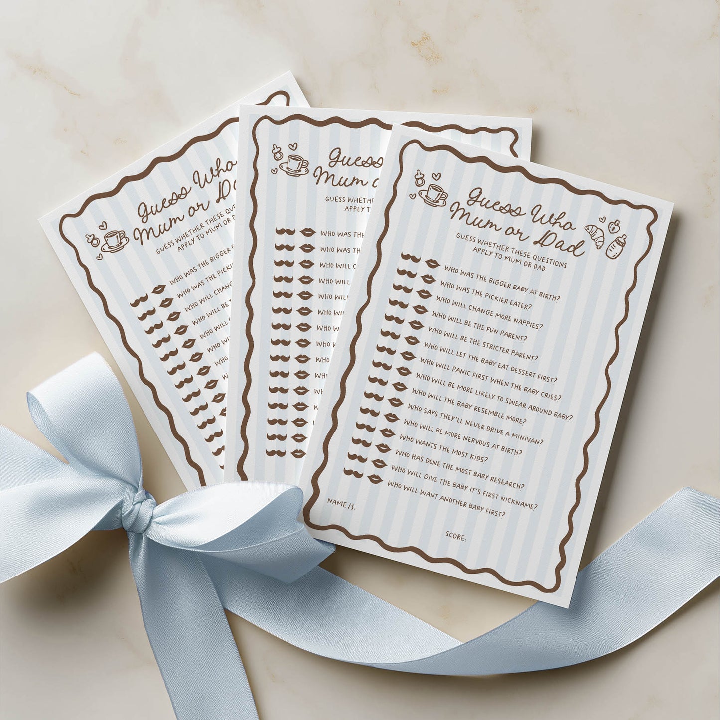 Three baby shower game cards with lip and mustache designs on a beige background with a blue ribbon.