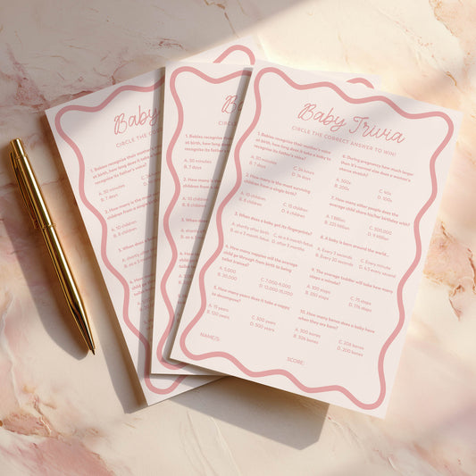 Three pink wavy baby shower game cards with a pen on a marble surface