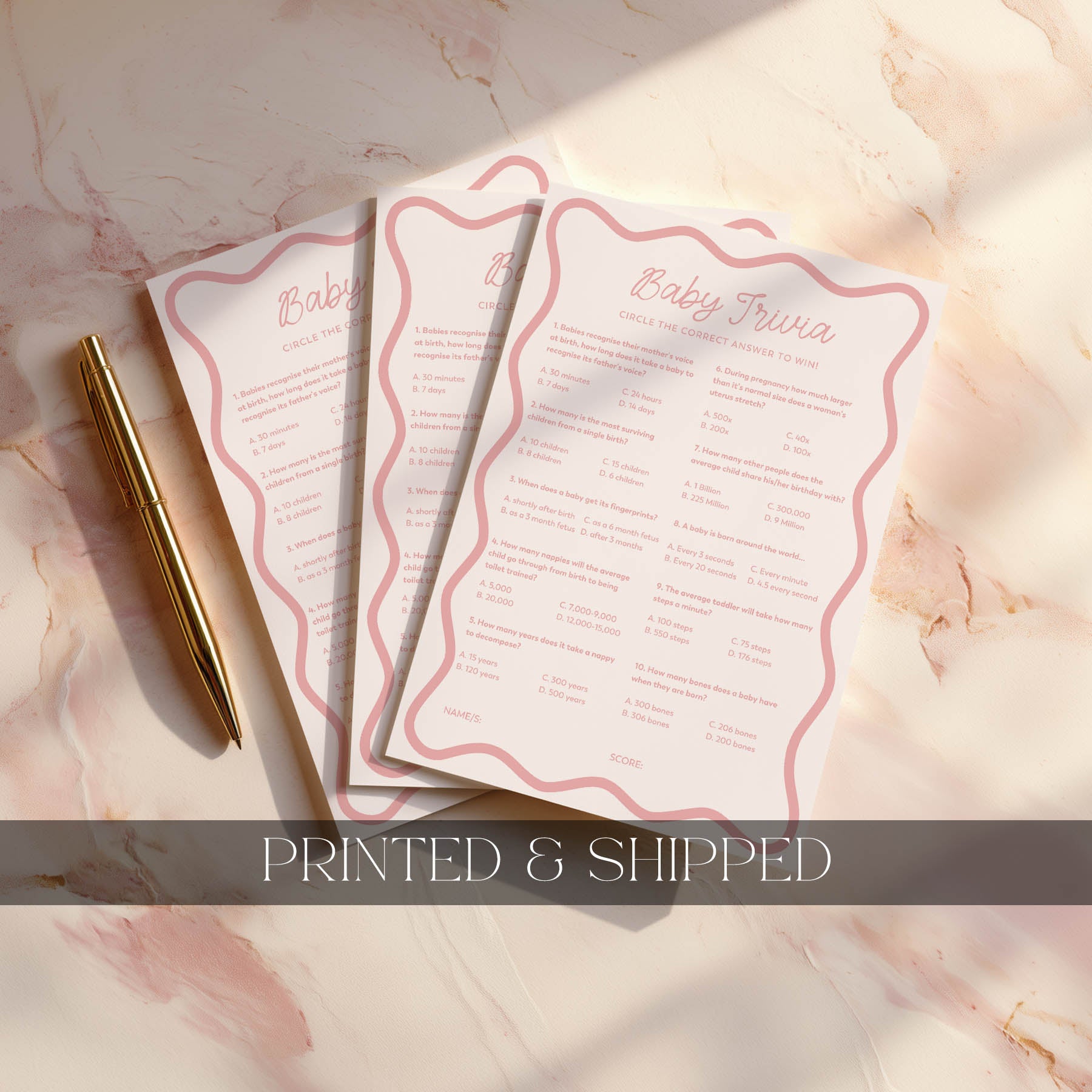 Three printed baby shower invitations on a marble surface with a gold pen.
