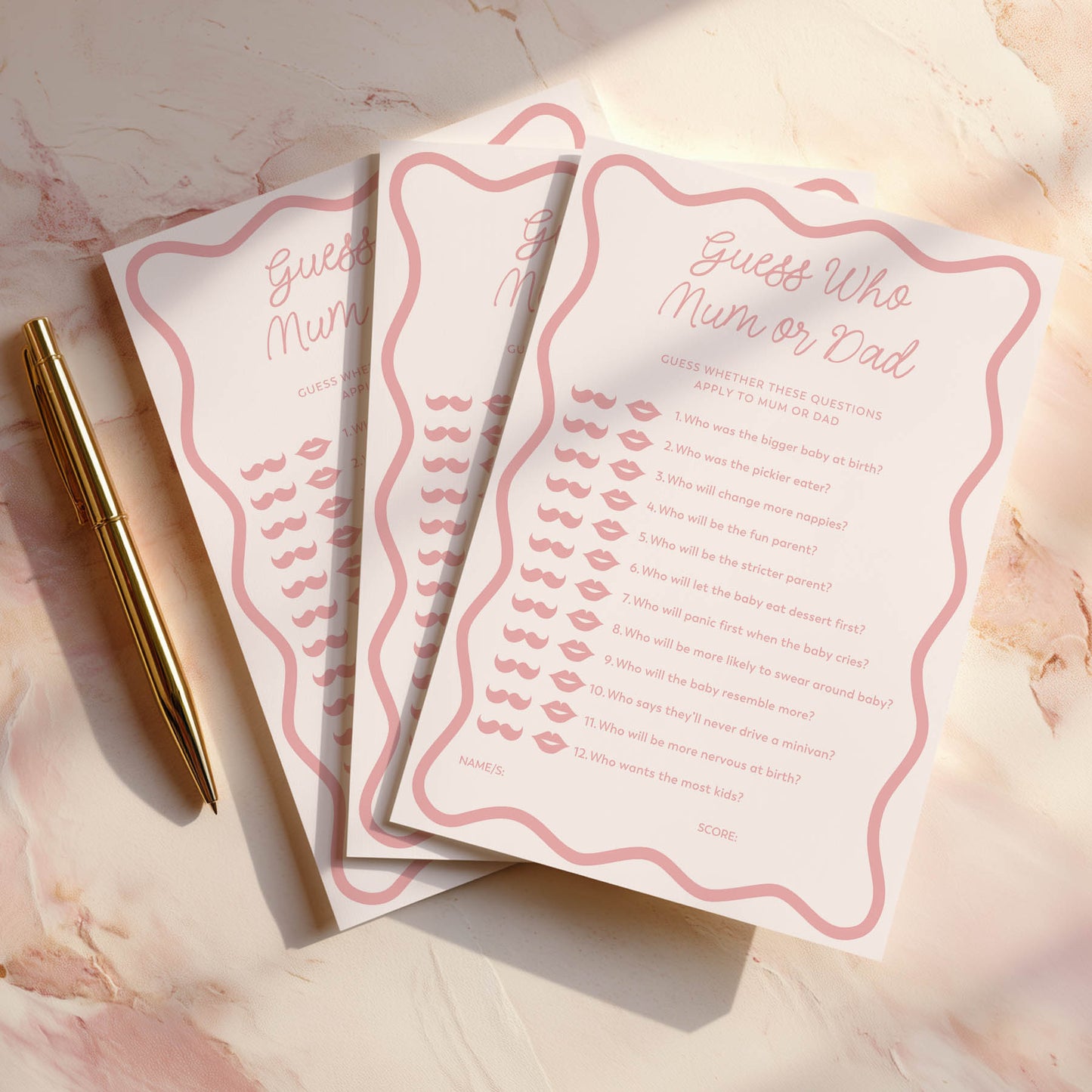Three pink wavy baby shower game cards with a pen on a marble surface