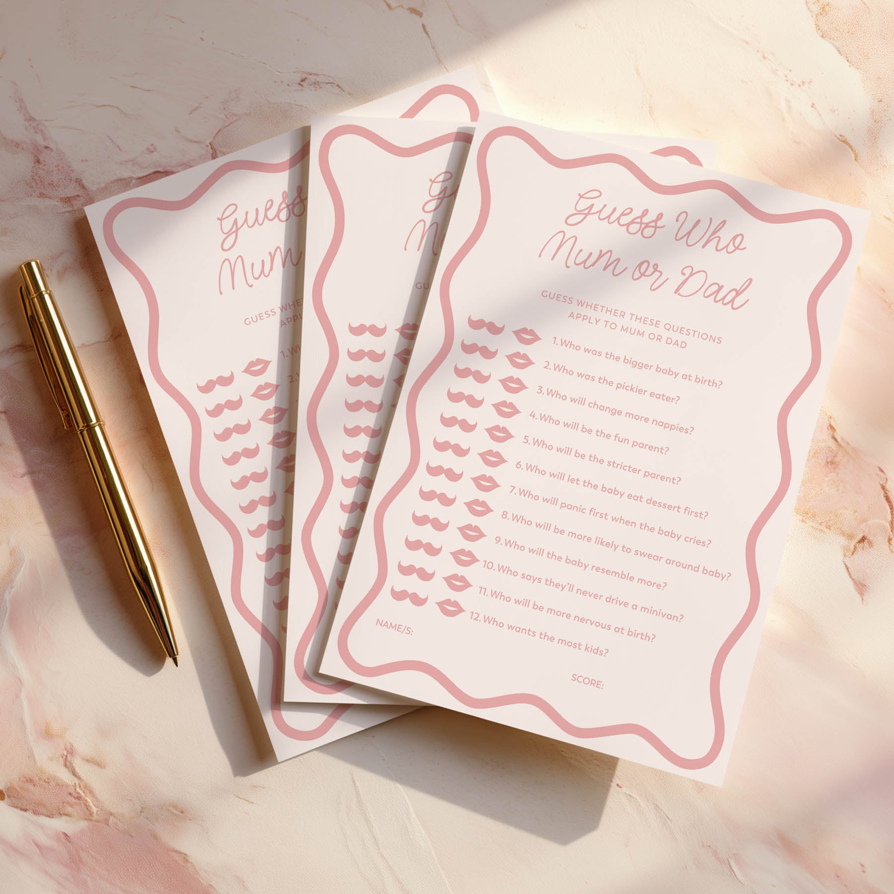 Three pink wavy baby shower game cards with a pen on a marble surface