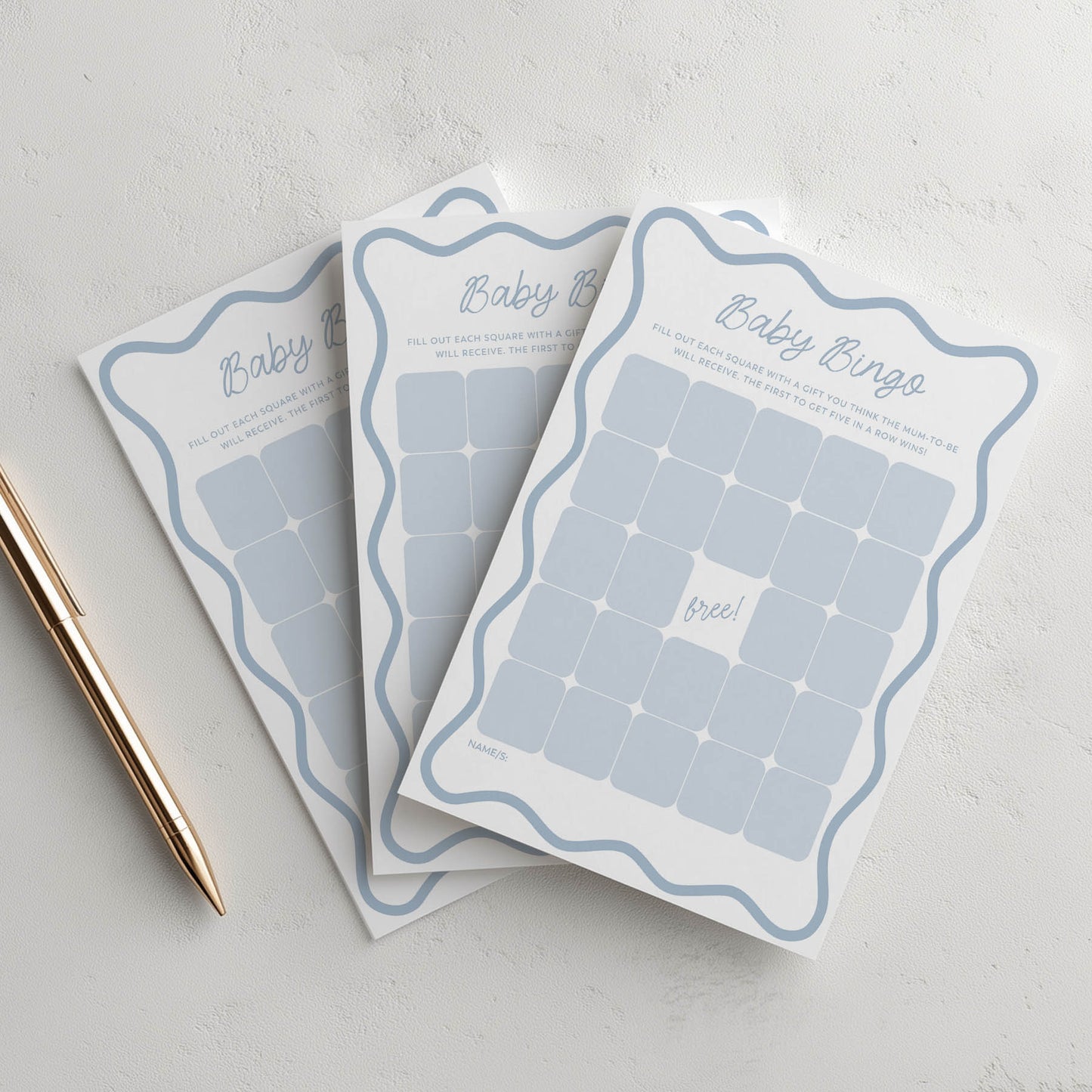 Three baby bingo cards on a light gray surface with a pen.