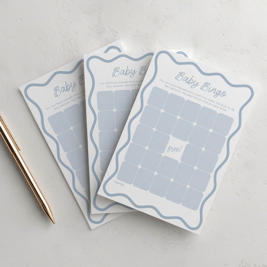 Three baby bingo cards on a light gray surface with a pen.