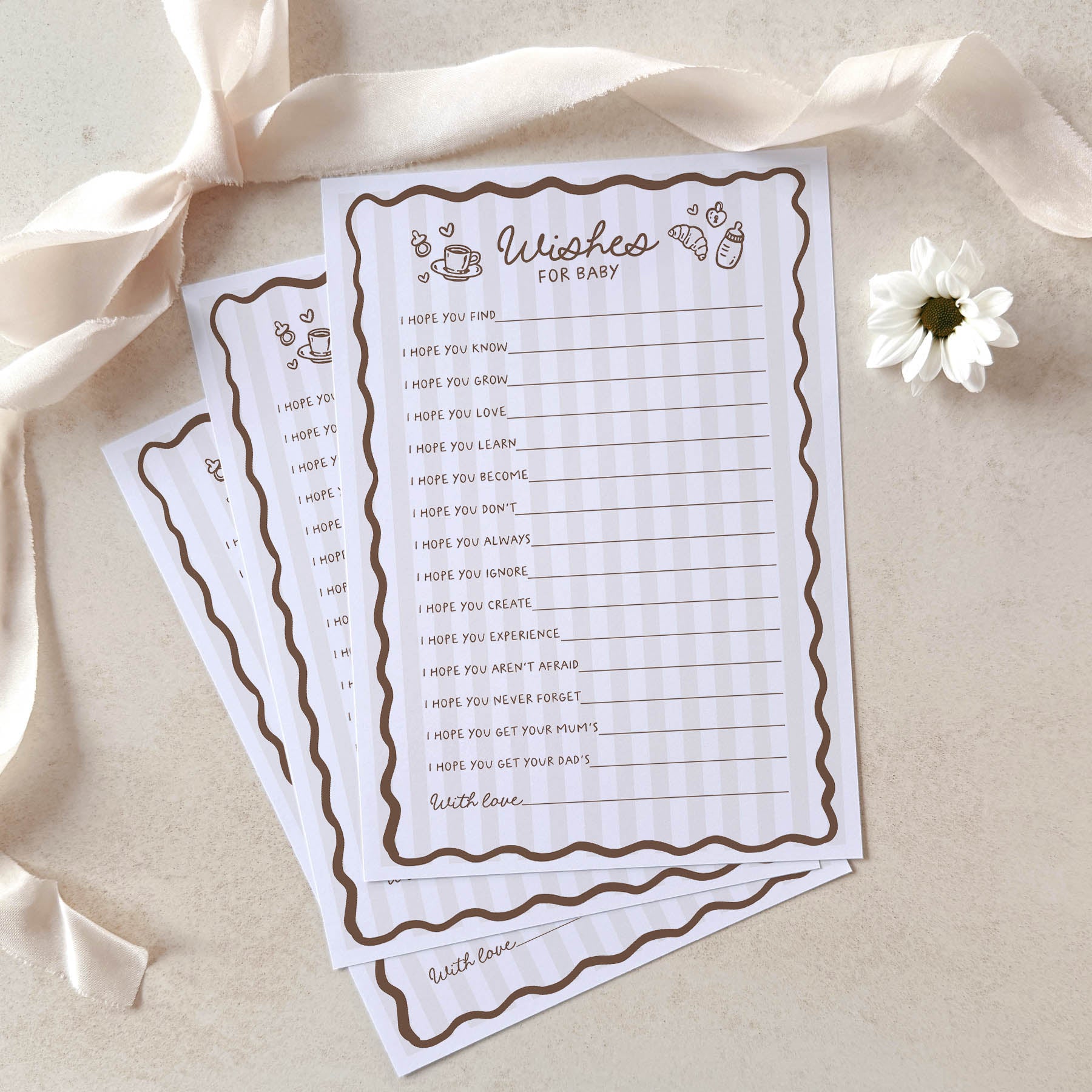 Two sheets of paper with a baby shower wish list on a beige background with ribbons and a flower.
