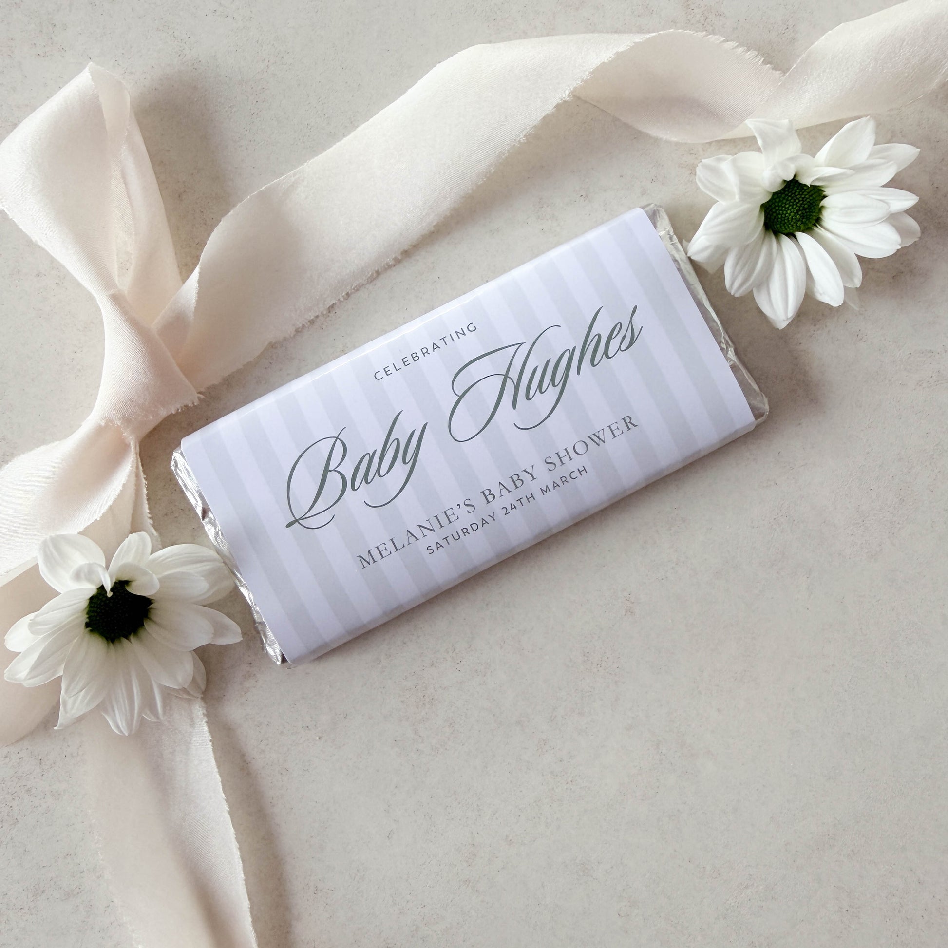Personalized baby shower chocolate bar with ribbon and flowers on a light background