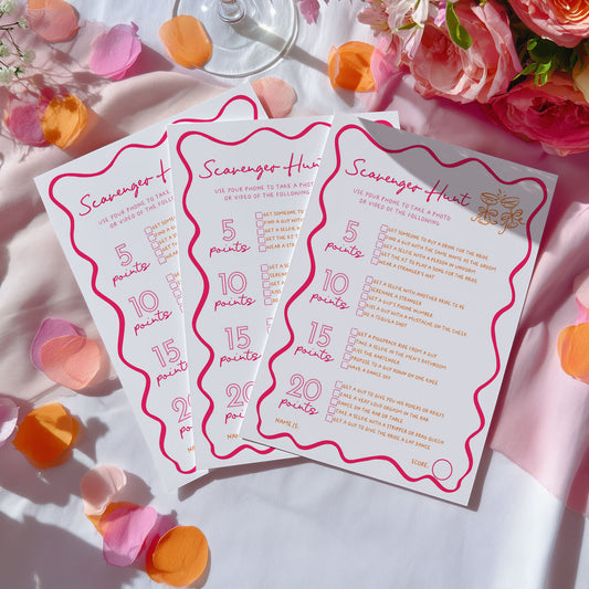 Three printed game cards titled "Scavenger Hunt" arranged on a white surface with pink rose petals, orange flower petals, and pink roses around them.