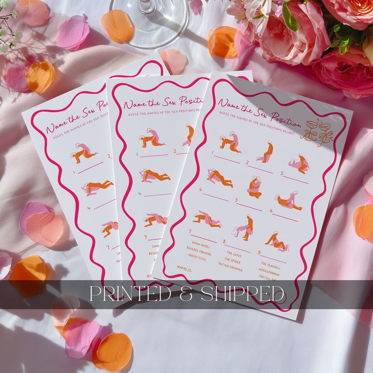 Three printed activity sheets titled "Name the Sex Position" are fanned out on a white fabric surface with pink and orange flower petals and a glass base visible around them. The sheets have pink wavy borders and small illustrated figures in orange, pink, and purple.