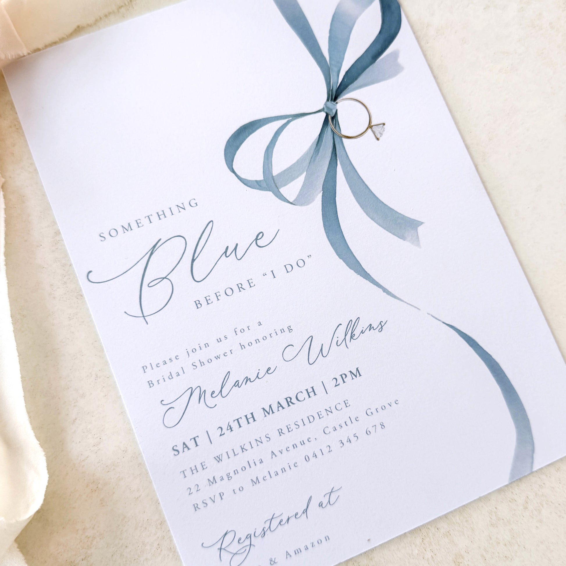 Wedding invitation with blue ribbon and ring on a beige fabric background