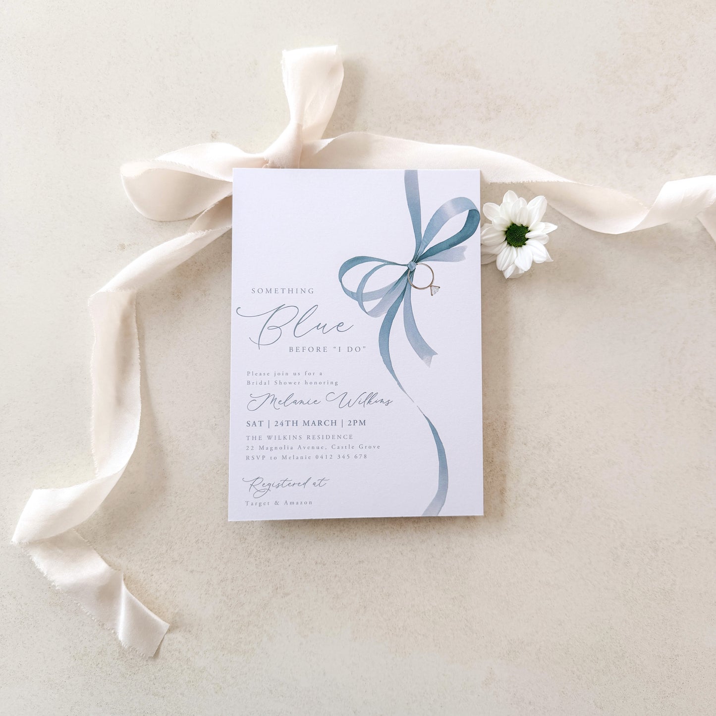 Wedding invitation card with a blue ribbon and white flower on a light background