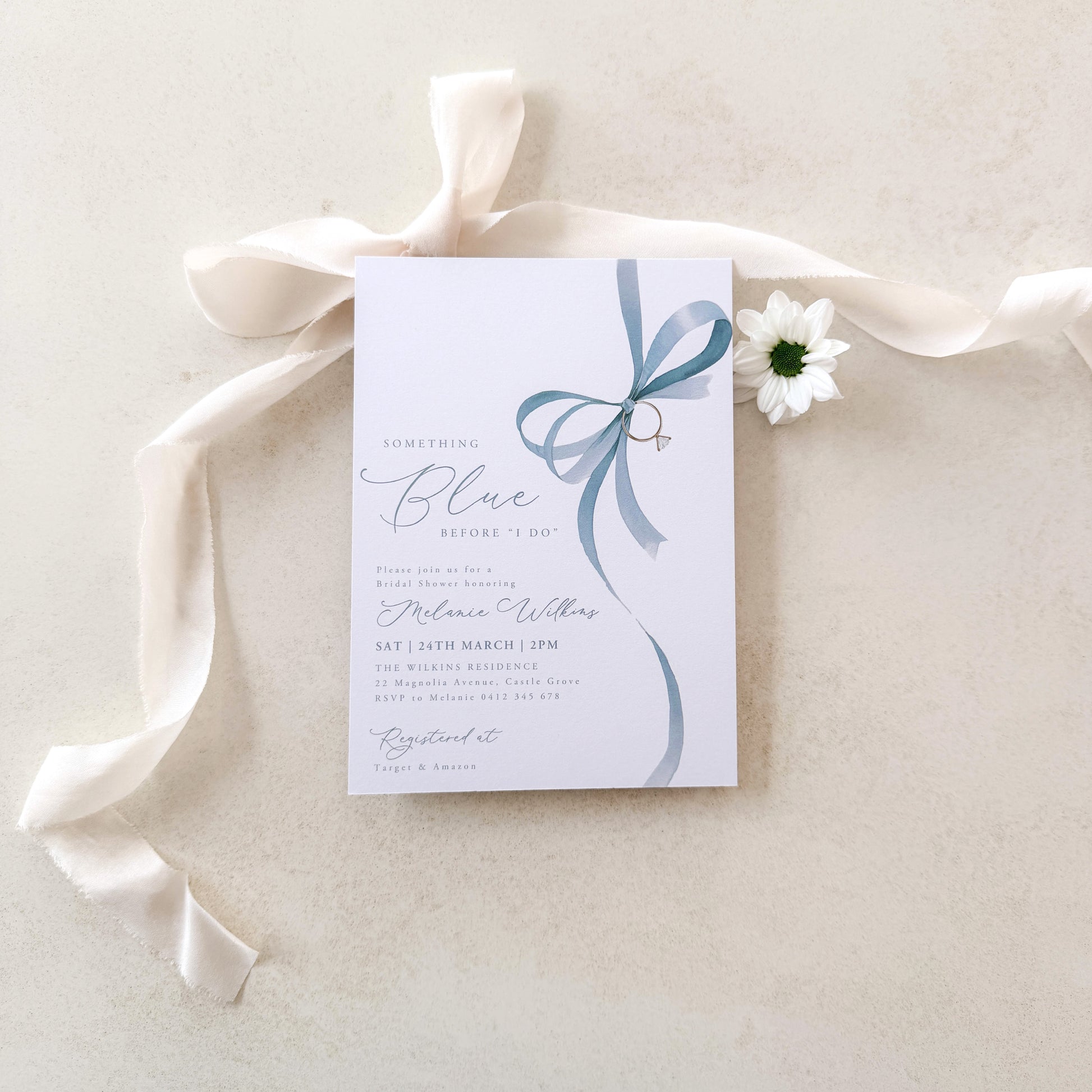 Wedding invitation card with a blue ribbon and white flower on a light background
