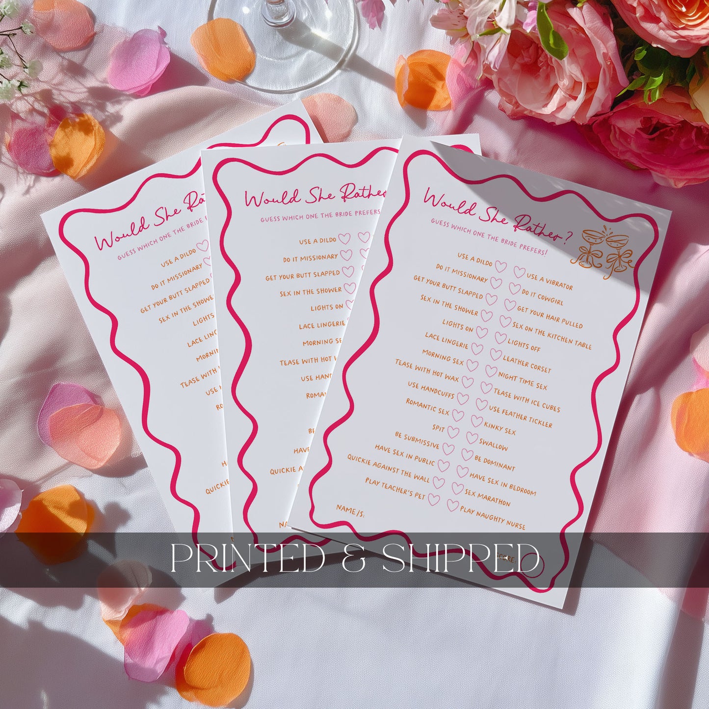 Three hens party games with pink wavy borders and rose gold script titles are arranged on a white surface with pink, peach, and orange flower petals. A glass stemware base is visible at the top, and a translucent banner at the bottom reads 'PRINTED & SHIPPED'.