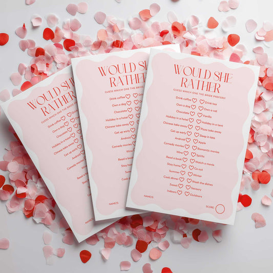 Three 'Would She Rather' cards on a surface with heart-shaped confetti.