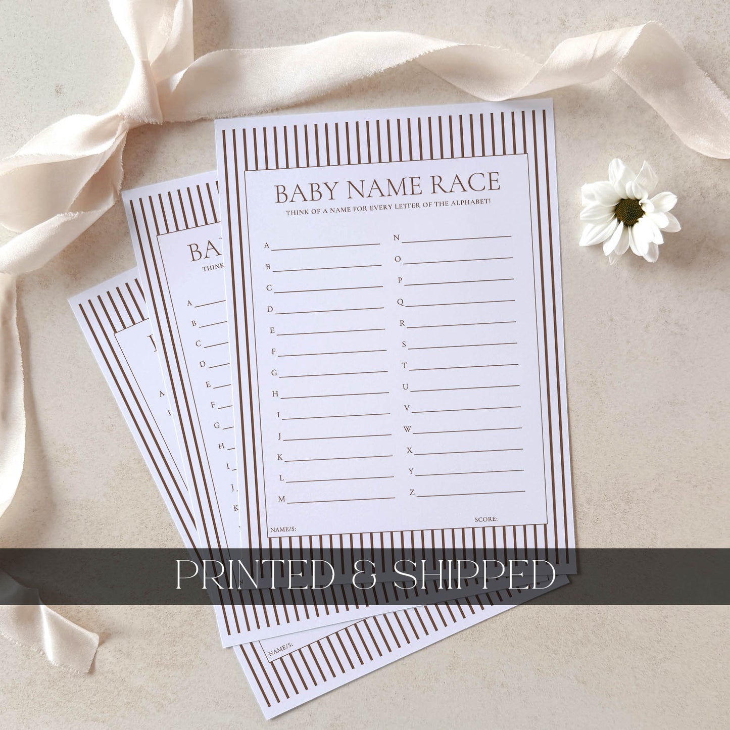 Two printed sheets with baby name games on a beige surface with ribbons and a flower.