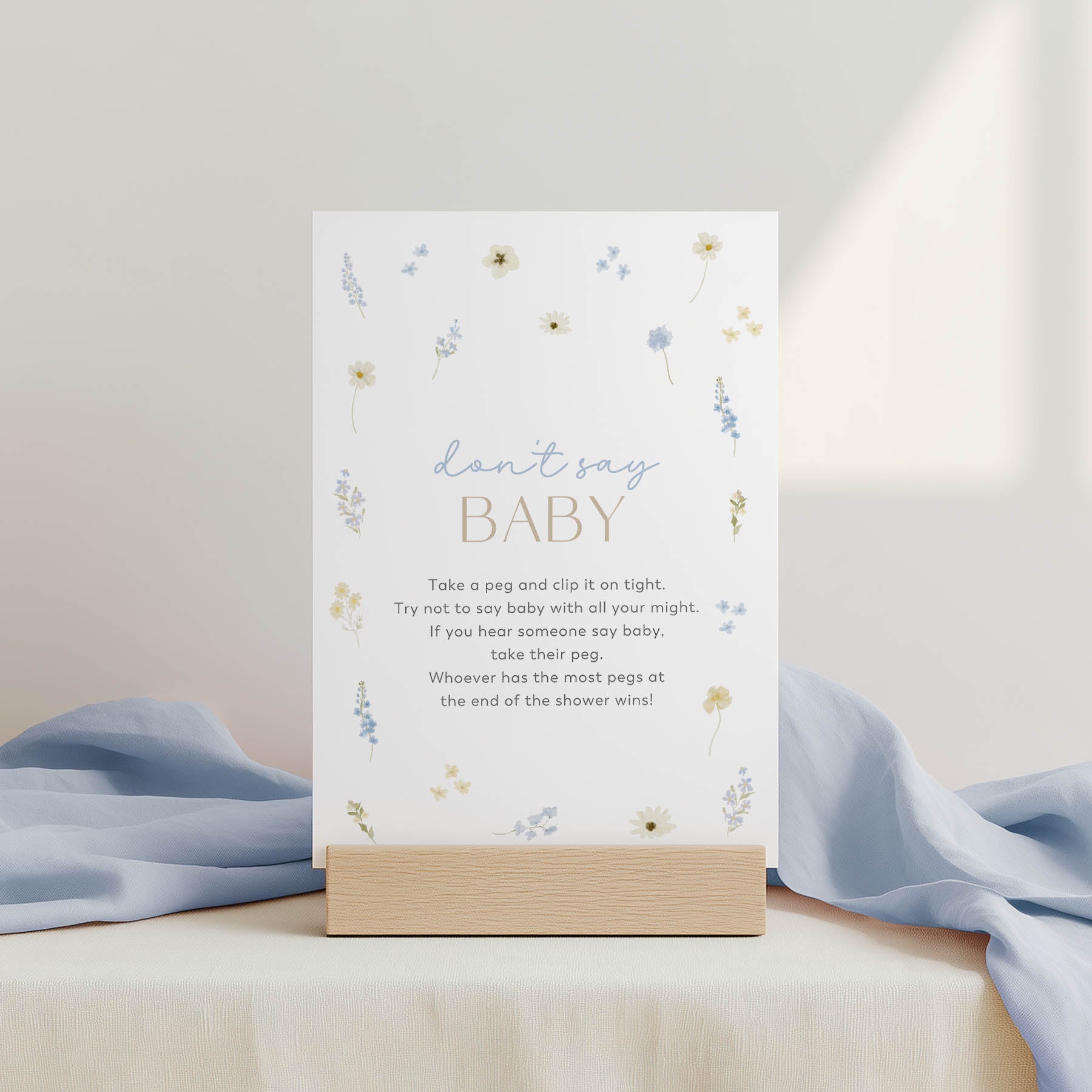 Baby shower game card with pegs and poem on a stand, surrounded by light blue fabric.