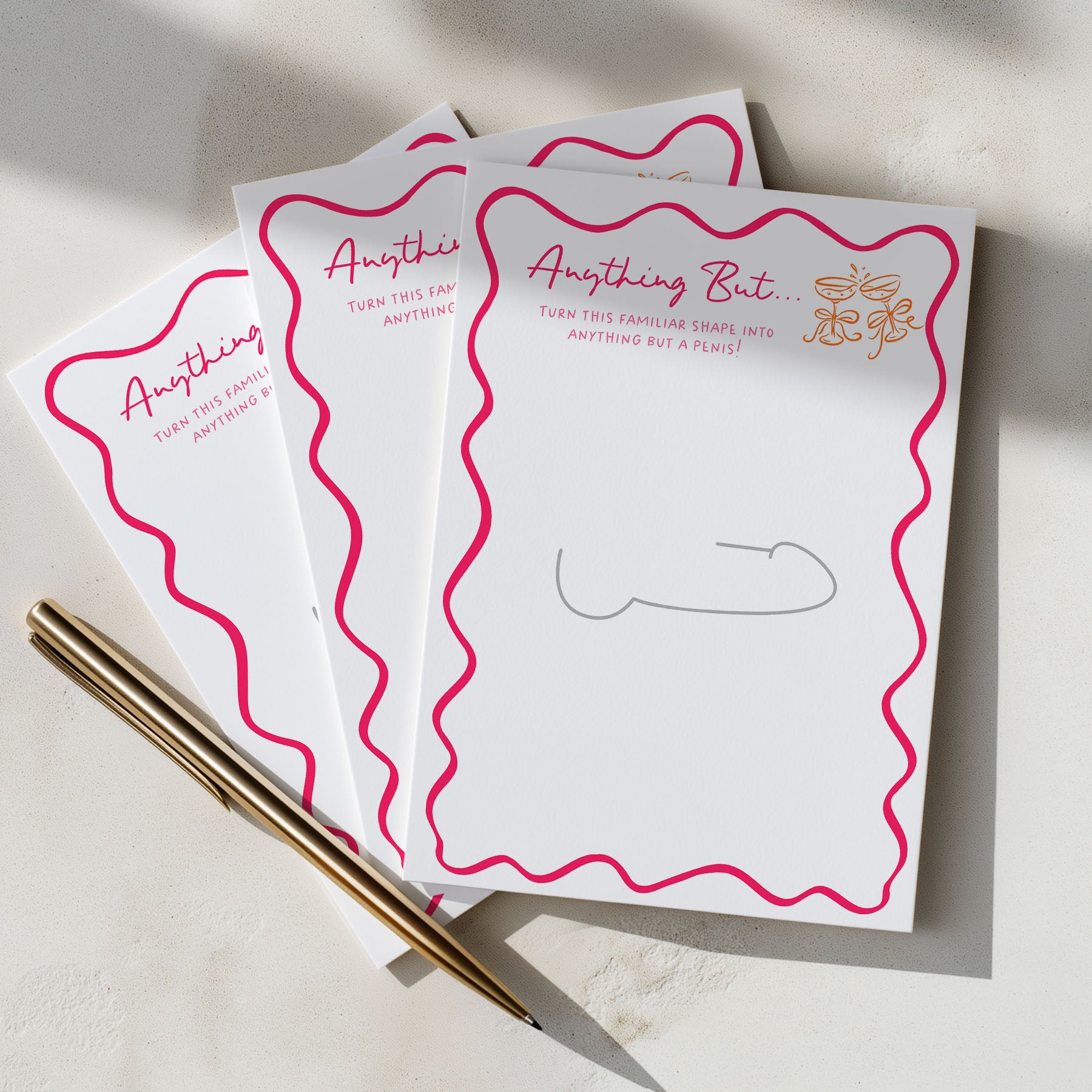 Three hens party anything but drawing game cards with pink wavy borders and gold text, arranged on a light surface next to a gold pen