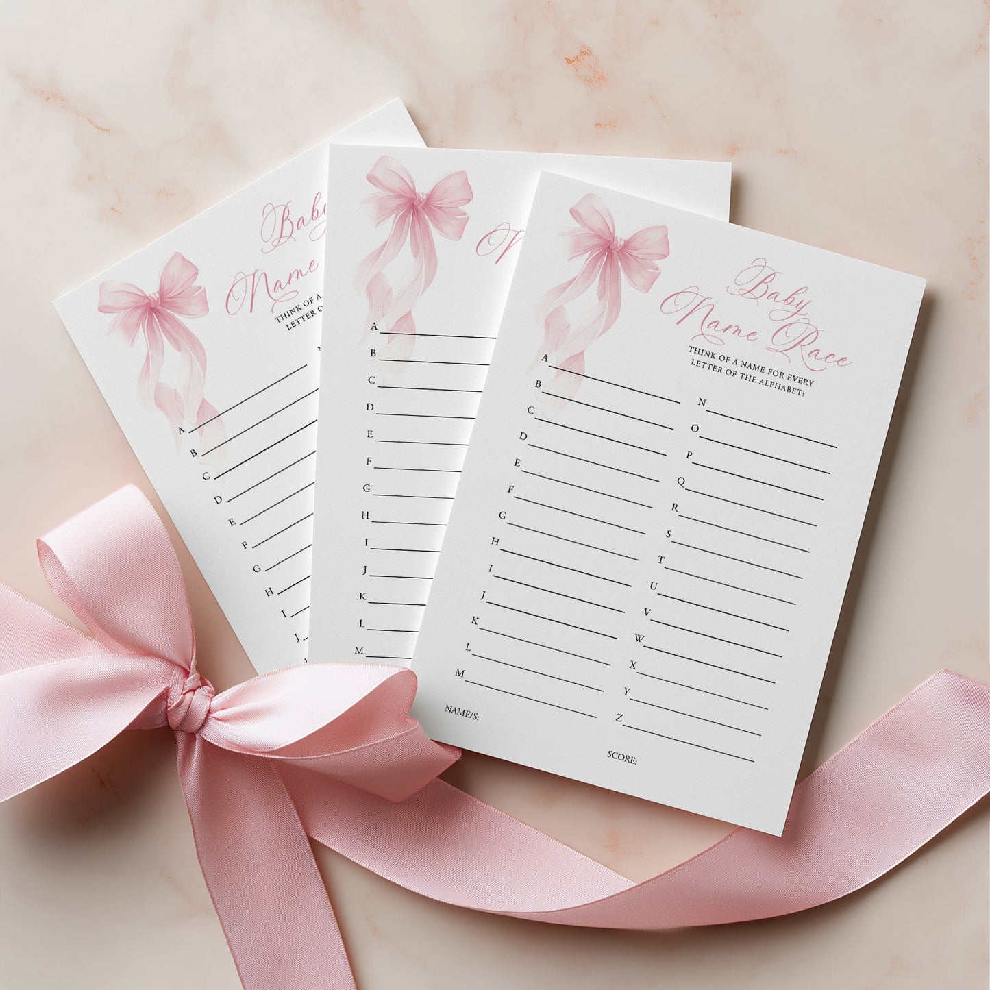 Three baby shower name place cards with pink ribbons on a light background