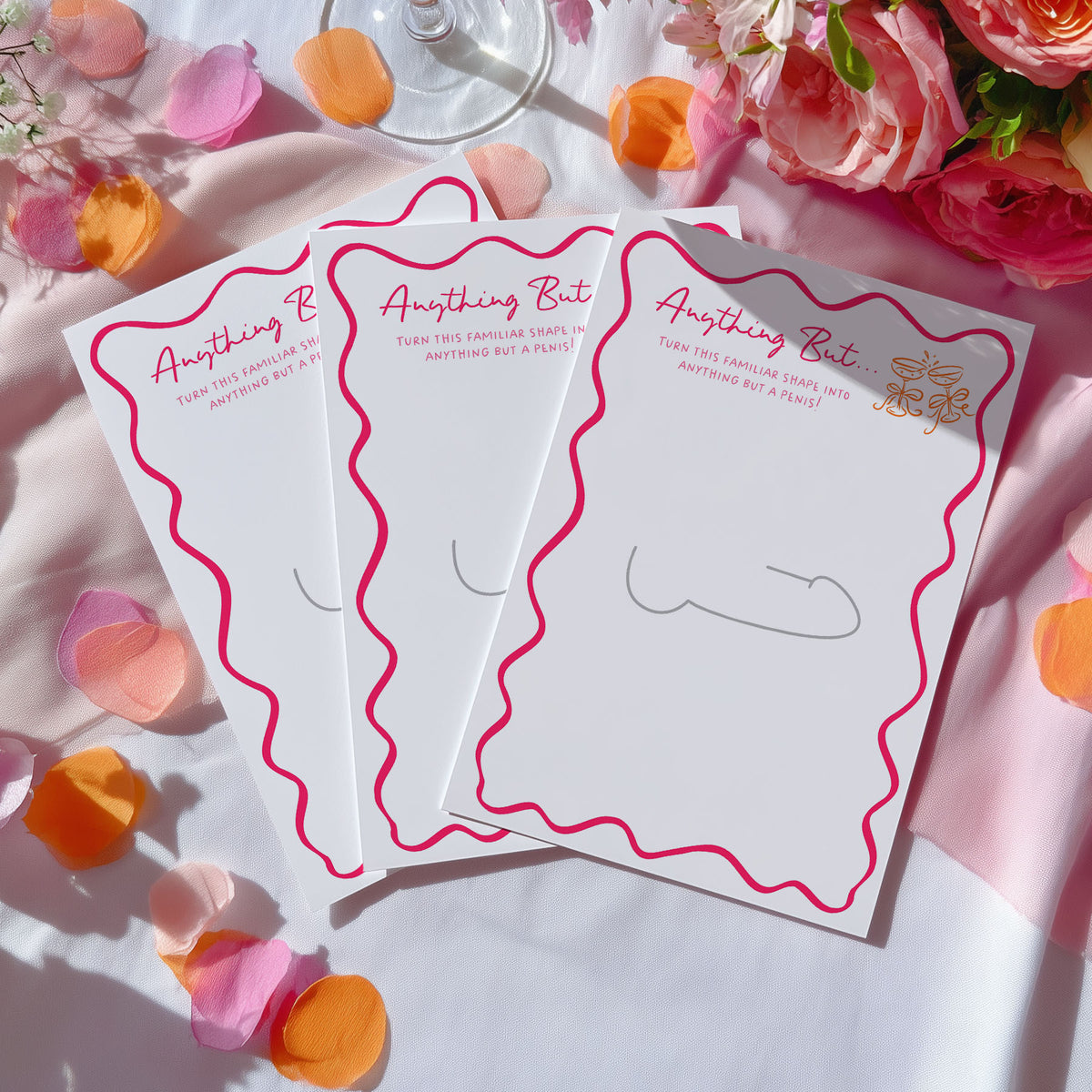 Three white notepad cards with pink wavy borders and the phrase 'Anything But' in pink script, arranged on a white fabric surface with pink and orange flower petals and flowers around them.