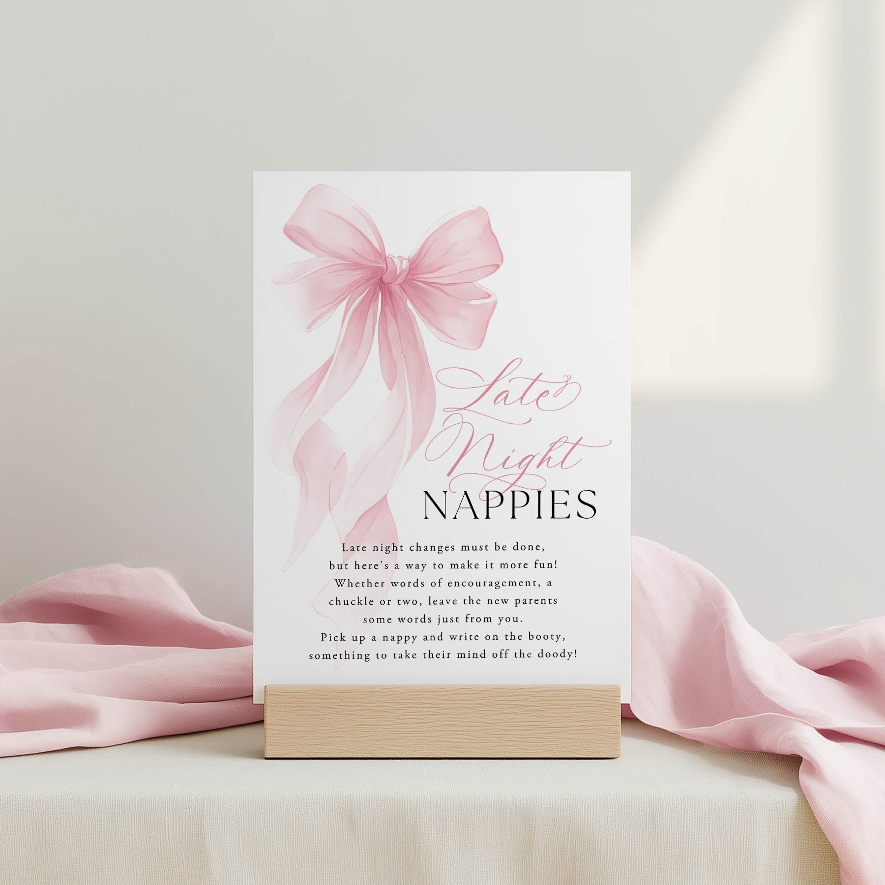 Card with pink bow and text on a stand, surrounded by pink fabric.